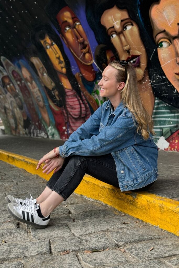 girl sat on the sidewalk with street art in the background